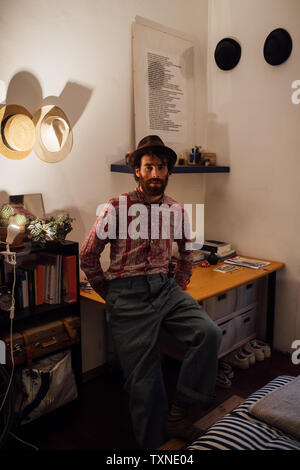 Bearded young man sitting on bedroom table Stock Photo
