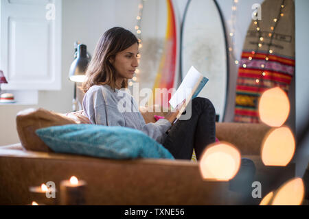 Young woman sitting on living room sofa reading a book Stock Photo