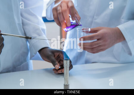 Young female and male scientists experimenting with liquid and bunsen burner in laboratory, cropped Stock Photo