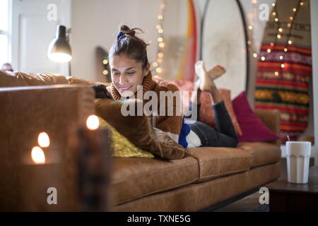 Young woman lying on living room sofa looking at laptop Stock Photo