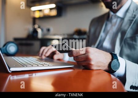 Mid adult man sitting at kitchen table with laptop and credit card, cropped