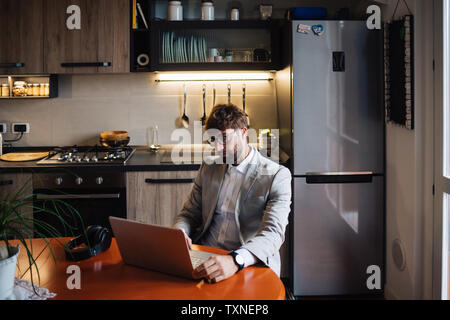 Mid adult man sitting at kitchen table typing on laptop Stock Photo