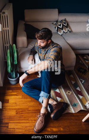 Mid adult man sitting on living room floor looking out through window