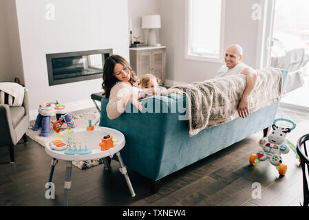 Mother and father reclining on sofa with baby daughter Stock Photo