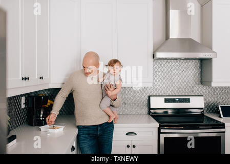 Father carrying baby daughter in kitchen, portrait Stock Photo