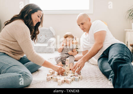 Mother and father on nursery floor with baby daughter playing with building blocks Stock Photo