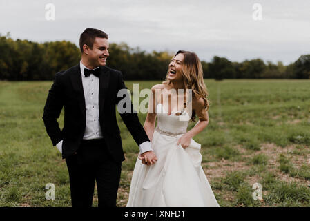 Romantic young bride and groom holding hands and laughing in field Stock Photo