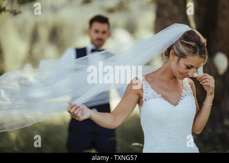Bride and groom holding delicate wedding veil in woodland Stock Photo