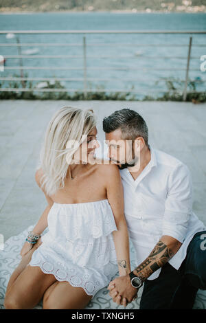 Romantic mid adult couple gazing at each other on lakeside, Stresa, Piemonte, Italy Stock Photo