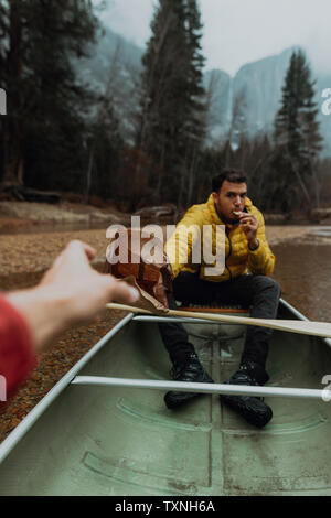Young canoeing couple sharing snacks on canoe, personal perspective, Yosemite Village, California, USA Stock Photo