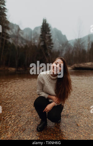 Young woman crouching in river, portrait, Yosemite Village, California, USA Stock Photo