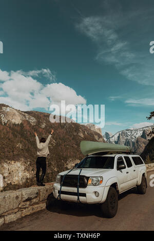 Young woman on top of roadside wall with hands raised, rear view, Yosemite Village, California, USA Stock Photo