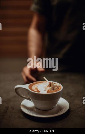 Barista at cafe counter with cup of mocha topped with toasted marshmallow, cropped shallow focus Stock Photo