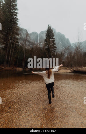 Young woman jumping in river shallows, rear view, Yosemite Village, California, USA Stock Photo
