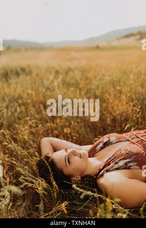 Beautiful young woman gazing up while lying in field of long grass, Exeter, California, USA Stock Photo