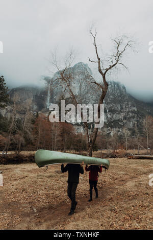 Young canoeing couple carrying canoe over heads in mountain landscape, Yosemite Village, California, USA Stock Photo