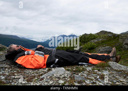Senior male hiker taking a break lying on top of mountain, side view, Valdez, Alaska, USA Stock Photo