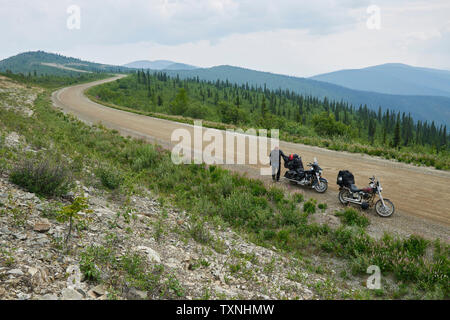 Senior male motorcyclist on rural mountain roadside with motorbike, high angle portrait, Dawson Creek, Canada Stock Photo