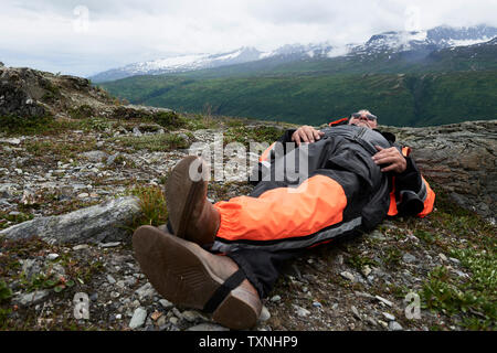 Senior male hiker taking a break lying on top of mountain, Valdez, Alaska, USA Stock Photo