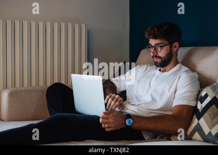 Mid adult man sitting on sofa typing on laptop Stock Photo