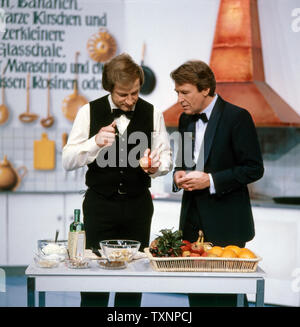 Günther Schramm, deutscher Schauspieler, Hörspielsprecher, Synchronsprecher, Fernsehmoderator, Kabarettist und Sänger in der ZDF Show 'Erkennen Sie die Melodie' mit Gastkoch Max Inzinger, Deutschland ca. 1980er. Günther Schramm, German actor, radio play speaker, dubbing artist, television presenter, cabaret artist and singer in the ZDF show 'Erkennen Sie die Melodie' with guest cook Max Inzinger, Germany ca. 1980s. Stock Photo