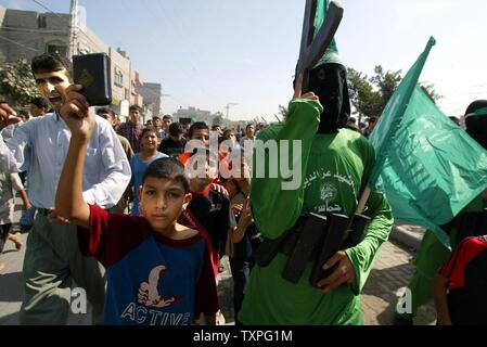 Masked members of Hamas' armed wing, Ezzedine al-Qassam Brigades, hold fake rifles and wear fake explosive belts during a rally in the Jabalya refugee camp in the southern Gaza Strip, on October 24, 2003. Palestinian militant groups Hamas and Islamic Jihad jointly claimed responsibility today for an overnight attack on a Jewish settlement in Gaza that left three Israelis and one of the gunmen dead. (UPI/Ismael Mohammad) Stock Photo