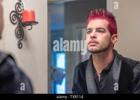 Diverse alternative caucasian male man with pink or purple spiked hair, gauged ears, gazing into the mirror, contemplating or thinking. Gay lgb, lgbt, Stock Photo
