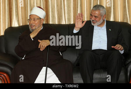 Hamas Prime Minister Ismail Haniyeh (R) and Egyptian Cleric and chairman of the International Union of Muslim Scholars Sheikh Yusuf al-Qaradawi waves to the crowd, upon al-Qaradawi's arrival at Rafah Crossing in the southern Gaza Strip May 8, 2013. Al-Qaradawi arrived on May 8, 2013 for a three-day visit to Gaza Strip with a delegation of Muslim scholars. UPI/Ismael Mohamad Stock Photo