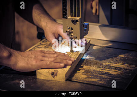 detail of a carpenter's hands using a band saw to cut a wooden plank Stock Photo