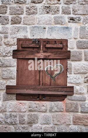 closed windows with brown wooden shutters with a painted heart, gray stone house Stock Photo