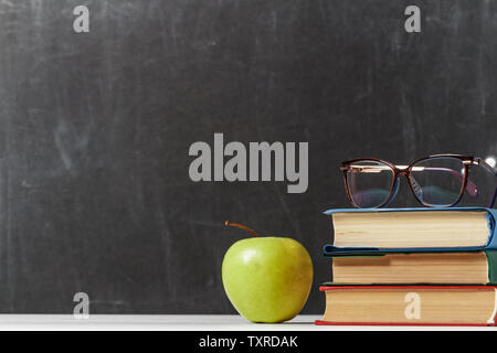 A stack of books, an apple, glasses on the background of a school blackboard. The concept of education. Copy space Stock Photo