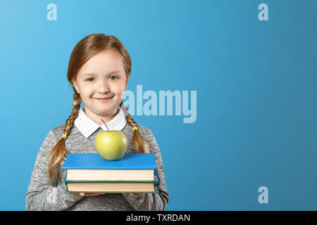 Portrait of a cheerful little girl on a blue background. Schoolgirl is holding a stack of books and an apple. Back to school. The concept of education Stock Photo