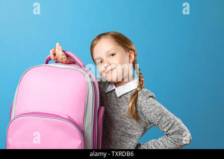 Closeup portrait of a little girl schoolgirl on a blue background. The child is holding a satchel. Back to school. The concept of education. Stock Photo