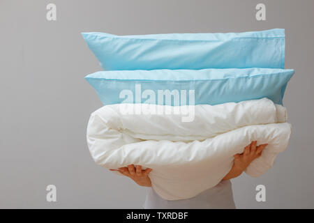 Woman holding a quilt and pillows on a background of gray wall. Stack bedding for sleep. Household. Stock Photo