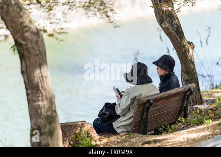 Uji, Japan - April 14, 2019: Spring in traditional village with people couple of women senior local friends sitting on bench with phone and view of ri Stock Photo