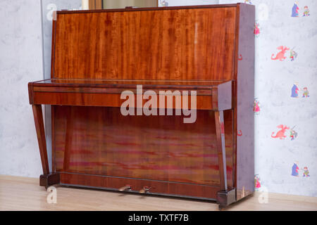 Old wooden piano keys on wooden musical instrument in front view . Old wooden piano. Brown piano stands against the wall . Stock Photo