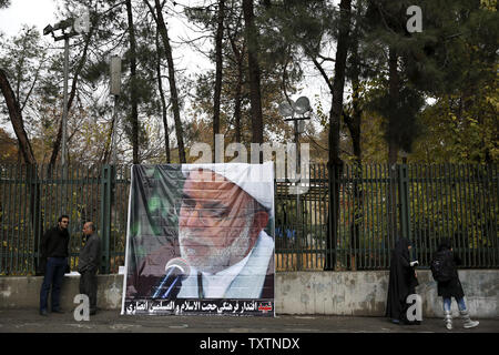 Mourners stand next to a big poster of  Iran's cultural attache, Ebrahim Ansari, during his funeral ceremony after Friday prayer in Tehran, Iran on November 22, 2013. Ansari was killed November 19, in a twin suicide attack outside the Iranian Embassy in a southern suburb of Beirut.     UPI/Maryam Rahmanian Stock Photo