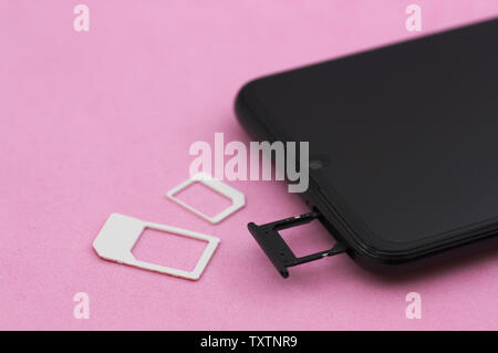 Remains of a SIM card and a smartphone with the tray for SIM cards open on a pink table Stock Photo