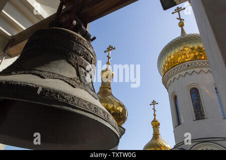 Donetsk, Ukraine - June, 16, 2019 year. View of the golden domes of the Trinity Сathedral from under the big bell on the bell tower in the Orthodox Ch Stock Photo