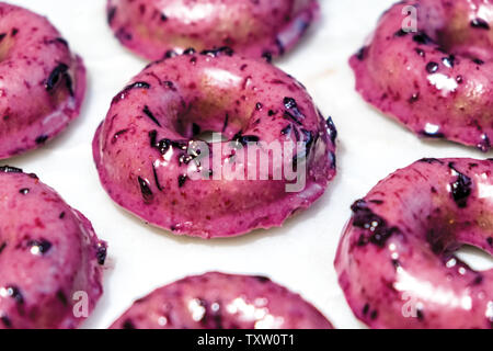 Freshly Baked Homemade Blueberry Doughnuts Dipped in Shiny Purple Blueberry Glaze with Chunks of Fresh Blueberries on a White Marble Surface Stock Photo