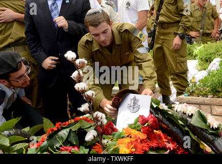 An Israeli soldier places a beret on the flower covered grave of American-Israeli soldier Max Steinberg, 24, at his funeral in the military cemetery on Mt. Herzl in Jerusalem, Israel, July 23, 2014.  Steinberg, a native of Los Angeles, California, immigrated to Israel and enlisted in the Israel Defense Forces in 2012, where he served as a sharpshooter in the elite Golani Brigade. He was among the 13 soldiers killed by Palestinian militants in the Gaza Strip on Sunday. Twenty-nine Israeli troops have been killed since the army launched a ground incursion into Gaza last week. More than 30,000 pe Stock Photo