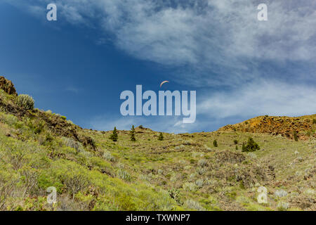 paraglider flying over the mountains peaks against the bright blue sky. Sunny day. Clear blue sky and some clouds above the mountains. Rocky tracking Stock Photo