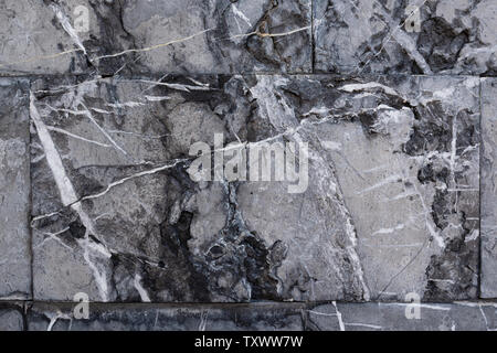Background from gray marble blocks. A wall of rough stone with black potholes and white lines Stock Photo
