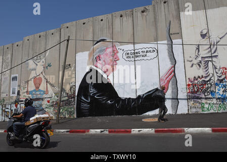 Palestinians past graffiti of U.S. President Donald Trump on Israel's controversial separation wall in the biblical city of Bethlehem, West Bank, August 9, 2017. The graffiti depicts Trump wearing a Jewish skullcap and thinking 'I'm going to build you a brother' in reference to the wall he has promised to build on the Mexican border.   -   Photo by Debbie Hill/UPI Stock Photo