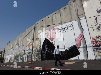 A Palestinian walks past graffiti of U.S. President Donald Trump on Israel's controversial separation wall in the biblical city of Bethlehem, West Bank, August 9, 2017. The graffiti depicts Trump wearing a Jewish skullcap and thinking 'I'm going to build you a brother' in reference to the wall he has promised to build on the Mexican border.   -   Photo by Debbie Hill/UPI Stock Photo