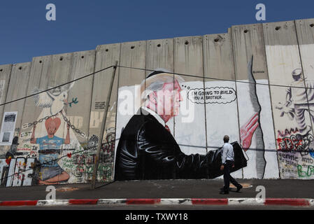 A Palestinian looks at graffiti of U.S. President Donald Trump on Israel's controversial separation wall in the biblical city of Bethlehem, West Bank, August 9, 2017. The graffiti depicts Trump wearing a Jewish skullcap and thinking 'I'm going to build you a brother' in reference to the wall he has promised to build on the Mexican border.   -   Photo by Debbie Hill/UPI Stock Photo