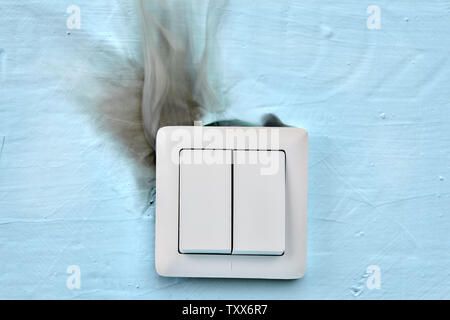 Old electrical wiring is dangerous, it can be a cause of fire in house. Smoke comes from light switch cover. Stock Photo