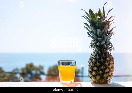 Pineapple juice in a glass and ripe pineapple on the background of the sea Stock Photo