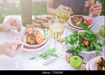 People eat in the garden at the table. Dinner concept with wine in the fresh air. Grilled sea fish and salads with vegetables and herbs. Mediterranean Stock Photo