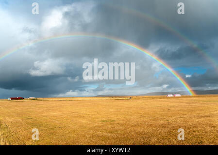 Rainbows against stormy sky over a grassy field in the countryside of Iceland in autumn Stock Photo